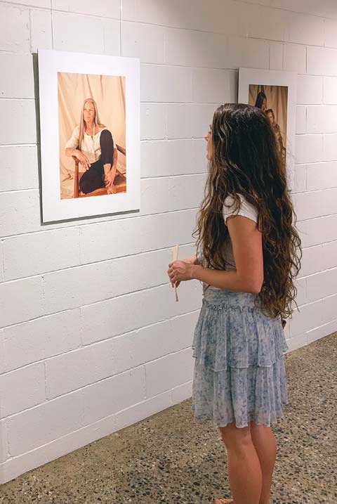 A woman with long dark hair looking at a photograph on display at an photography exhibit