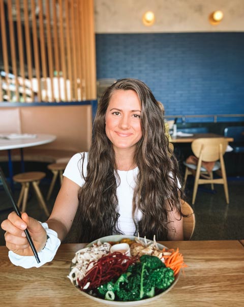 A brown-haired woman sitting at a table eating a gluten-free bowl of poke at Cheeky Poke in Brisbane