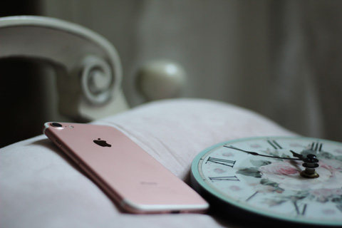 An iphone on a bed with a clock next to it